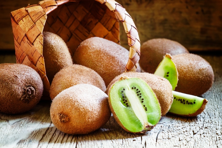 Kiwifruit poured out of a wicker basket, vintage wooden background, selective focus