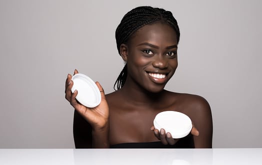 Laughing woman with moisturizing cream on her face. Photo of african american woman with flawless skin on white background. Skin care and beauty concept