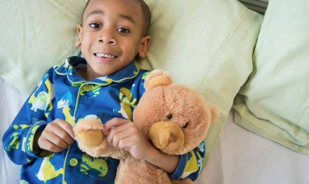 A little boy holding his teddy bear and wearing his pajamas in his bed