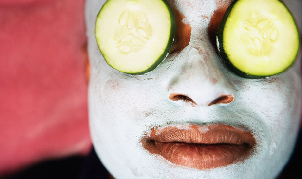 A man wearing a facial mask and cucumber slices over his eyes