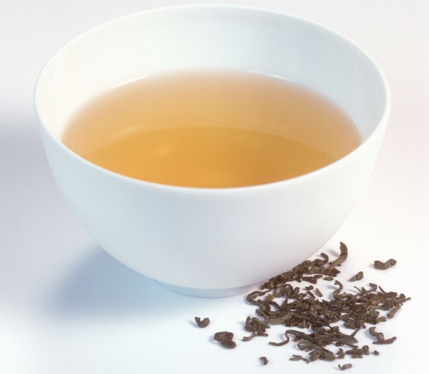 A cup of green tea with loose tea leaves beside it