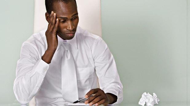 A sick man sitting at his desk and looking at a crumpled piece of tissue