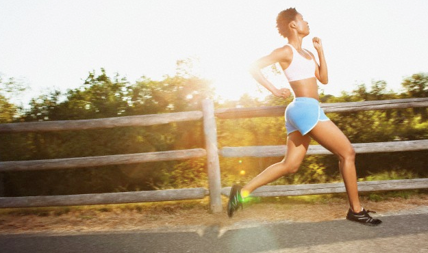 A woman in shorts running outside with the sun in the distance