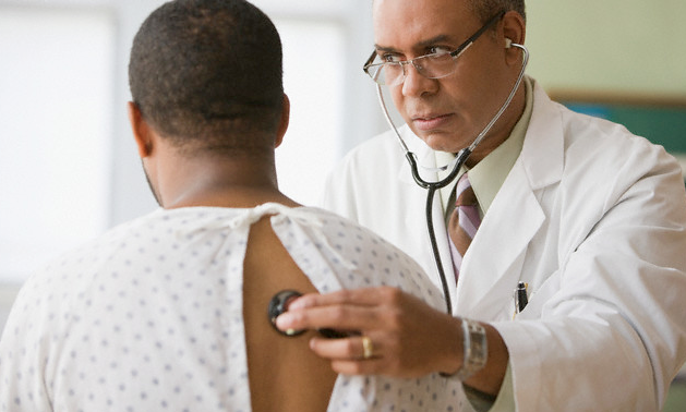 A doctor pressing a stethoscope against his male patient's back