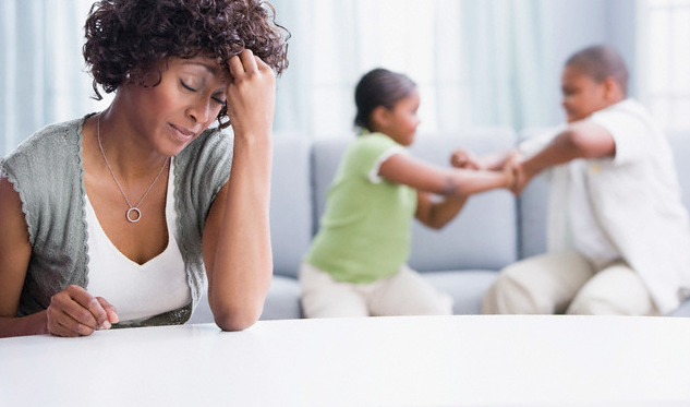 A mother with a headache, two children fighting in the background
