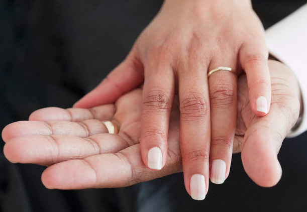 A married couple's hands on top of each other, both wearing wedding rings