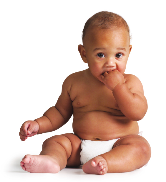 an african american baby sits in a diaper and puts his hand in his mouth