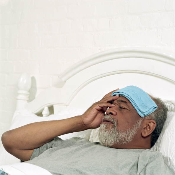 Senior man lying in bed, holding flannel to forehead, close-up