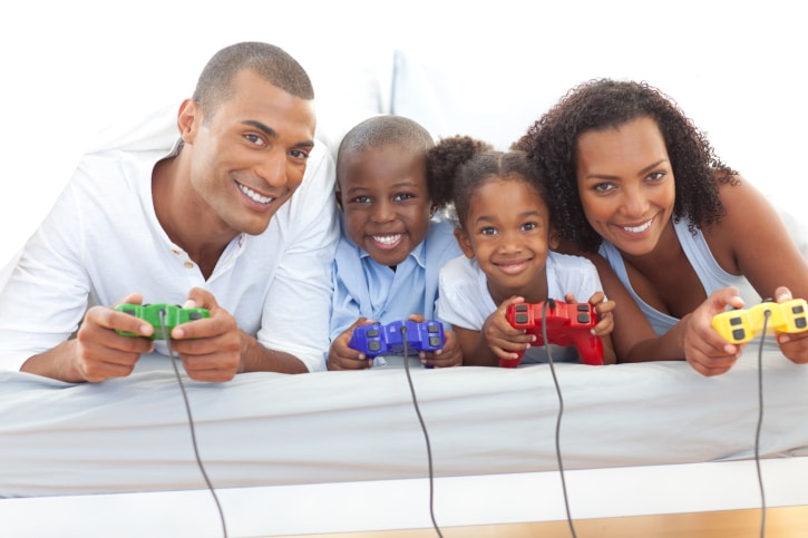African American Black Animated family playing video game lying down on bed