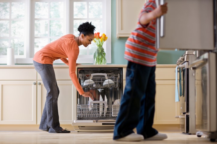 African American Black Woman Unloading Dishwasher While Son Looks in Refrigerator in kitchen