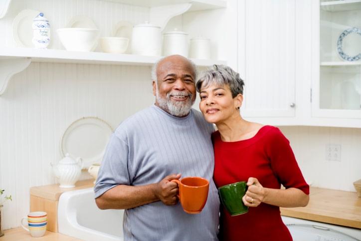 African American senior couple in kitchen hugging with coffee mugs
