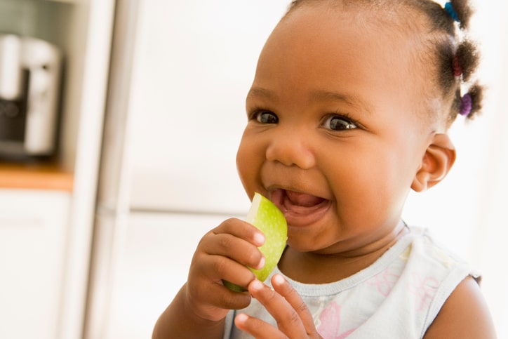 African American baby girl eating apple slice