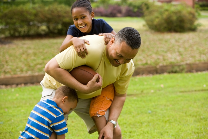 African American father playing outside with children