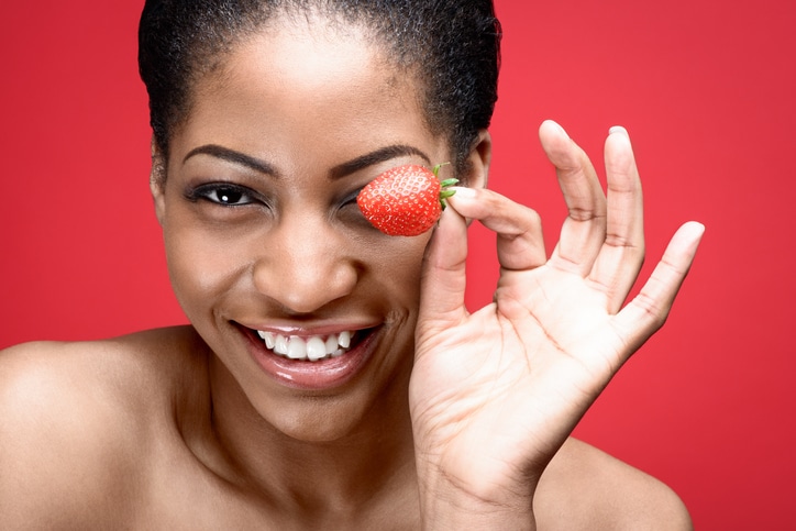 African American woman holding strawberry by eye