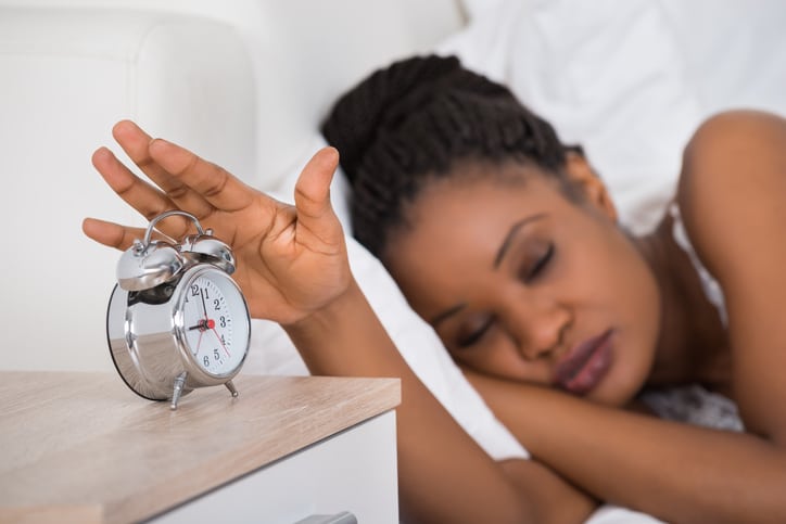 African American woman sleeping in bed hitting alarm