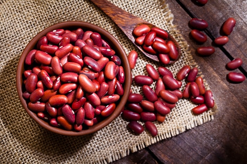 Top view of a brown bowl filled with Kidney beans shot on rustic wood table. A wooden spoon is beside the bowl with some beans on it. DSRL studio photo taken with Canon EOS 5D Mk II and Canon EF 100mm f/2.8L Macro IS USM